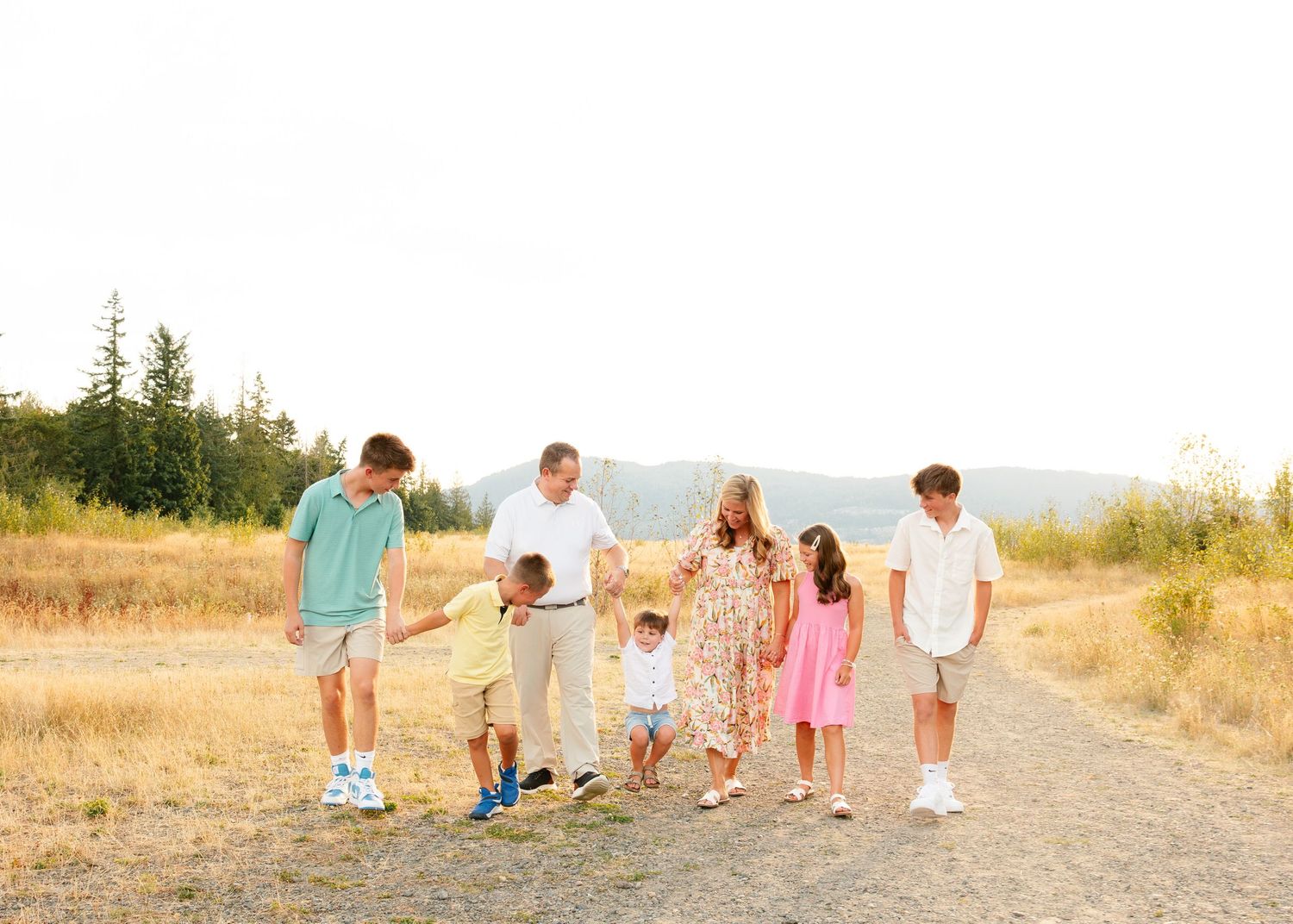 A baby wearing a green shirt sits on a beige blanket in a sunlit field during golden hour.