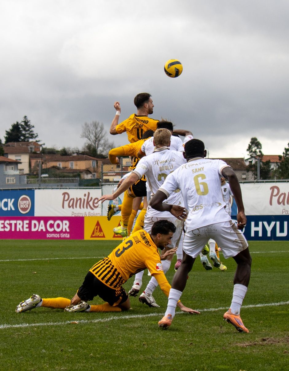 Intense soccer match action with players in yellow and white uniforms competing for the ball.