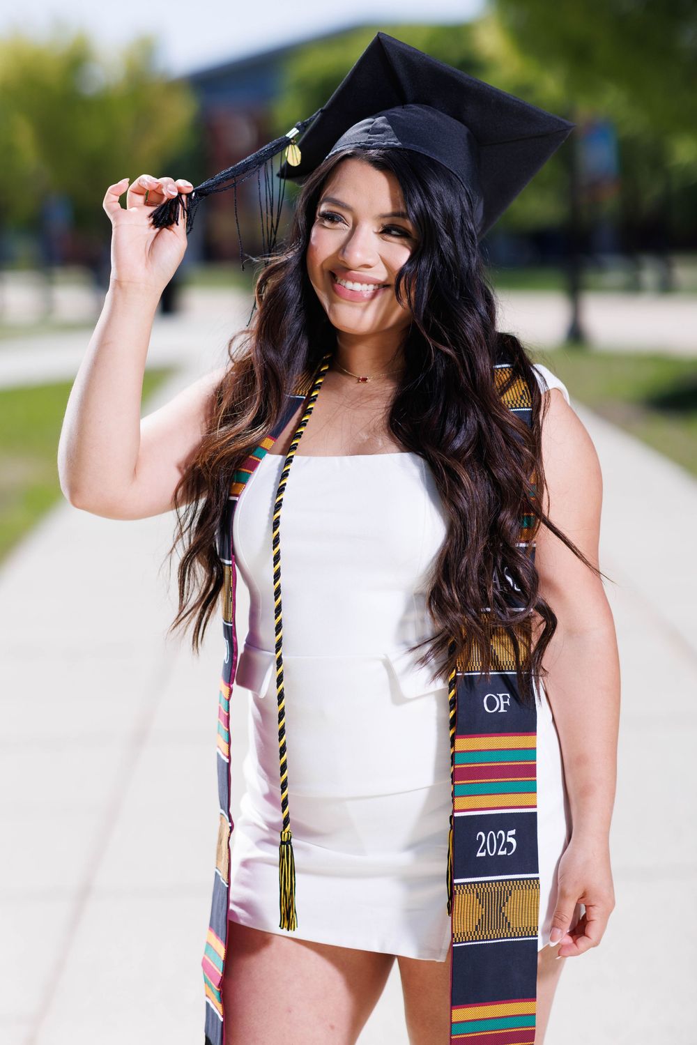 Graduate in white top and graduation cap poses for celebratory photos outdoors.