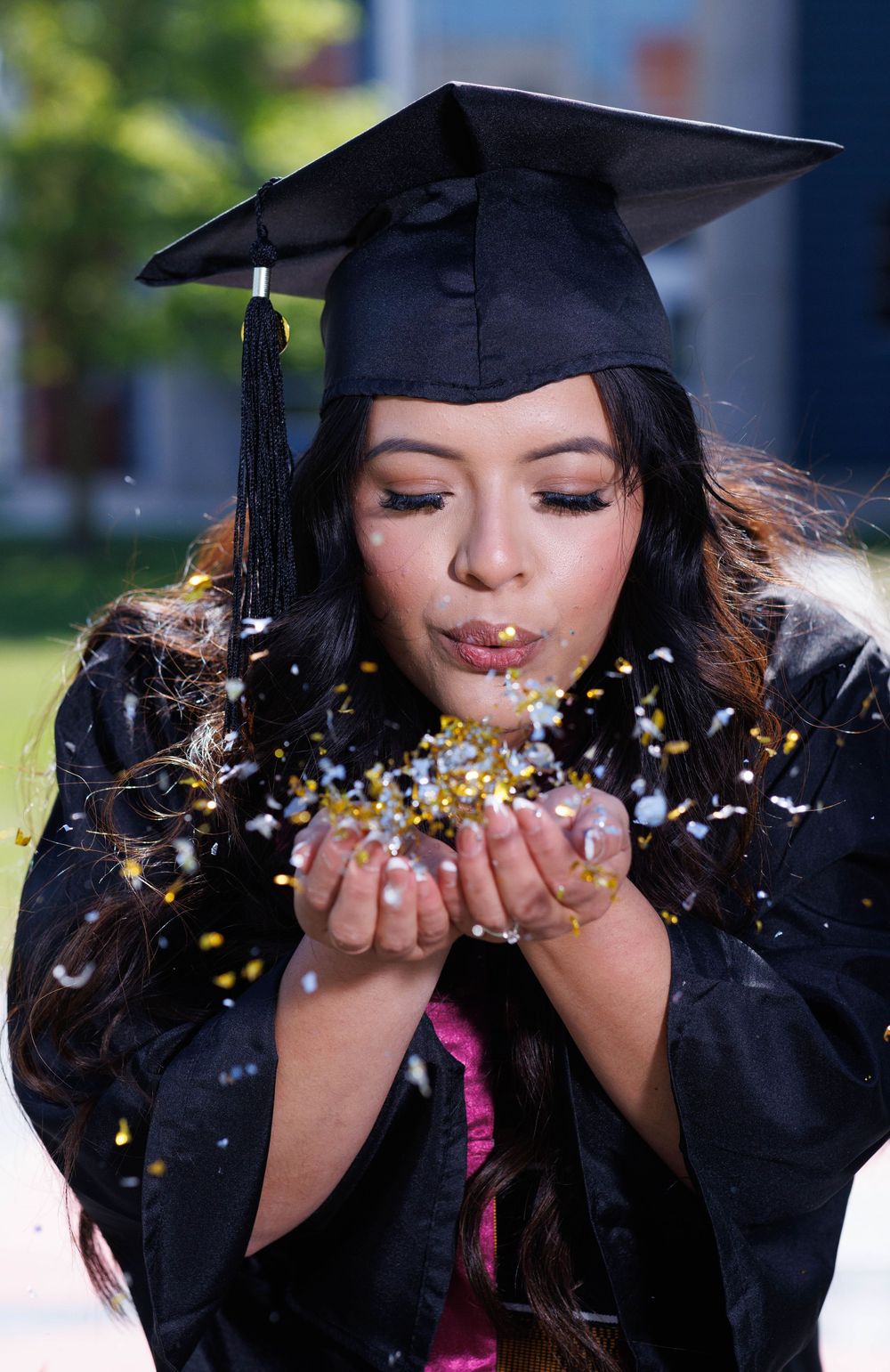 Graduate blows glitter confetti during outdoor graduation photoshoot.