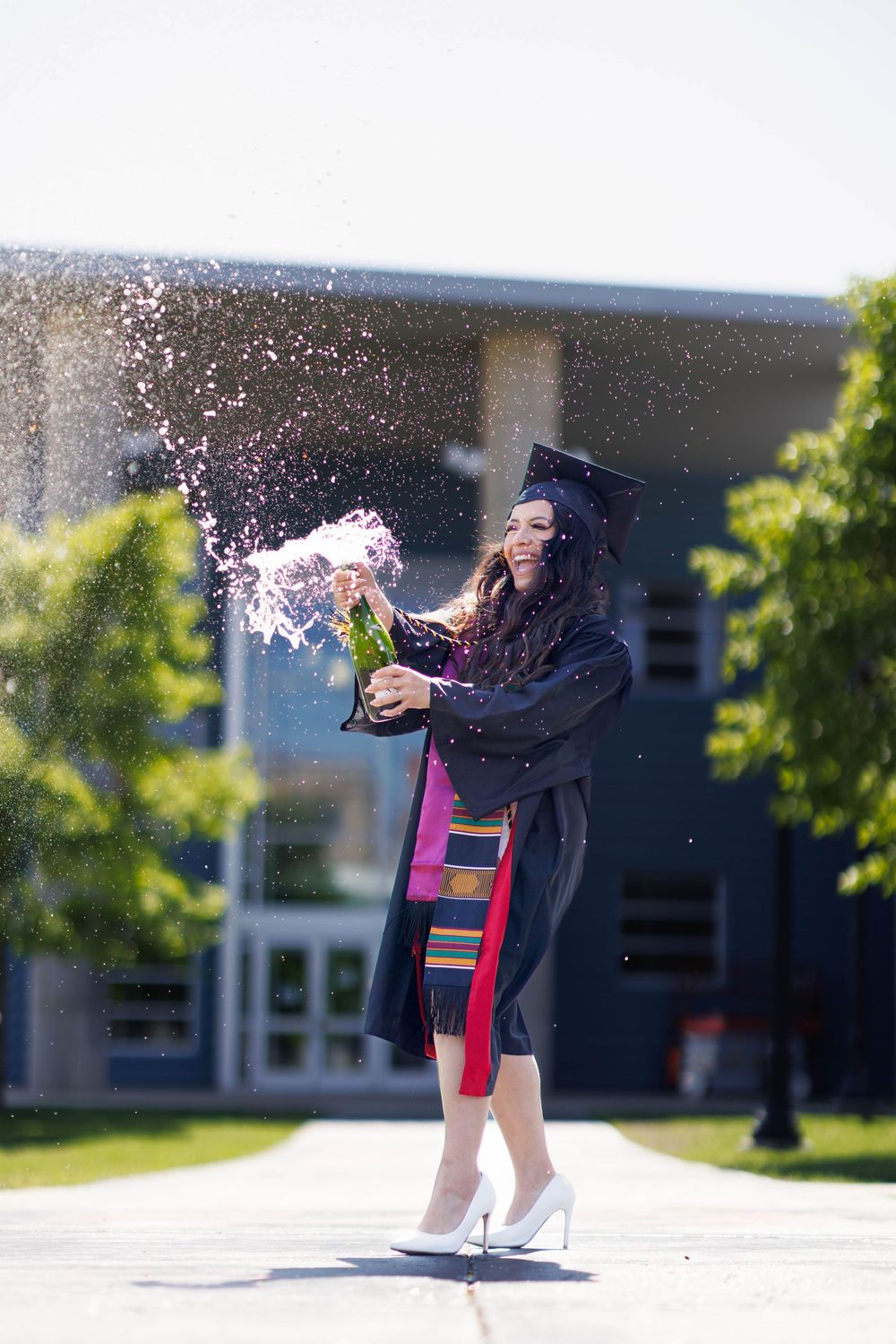 Graduate celebrates with glitter toss in front of campus building.