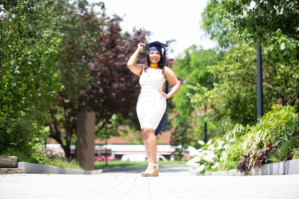 Graduate poses in outdoor garden setting wearing academic regalia.