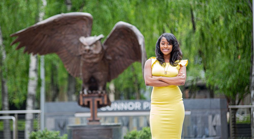 Woman in bright yellow dress poses outdoors for graduation photos in a park setting.