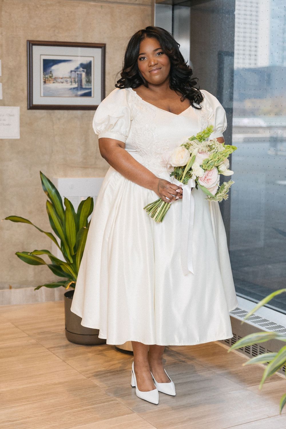 Elegant white dress with short sleeves and a flared skirt paired with white heels and a small floral bouquet.