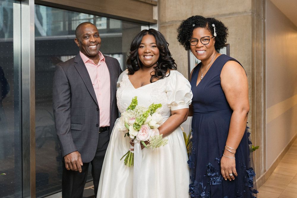 A wedding party poses together in a modern hallway with white flowers and formal attire.