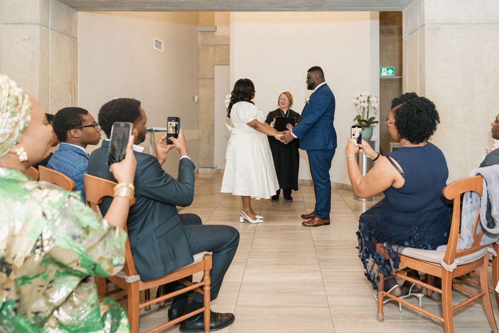 Wedding ceremony guests capture photos of a couple exchanging vows in an elegant indoor venue.