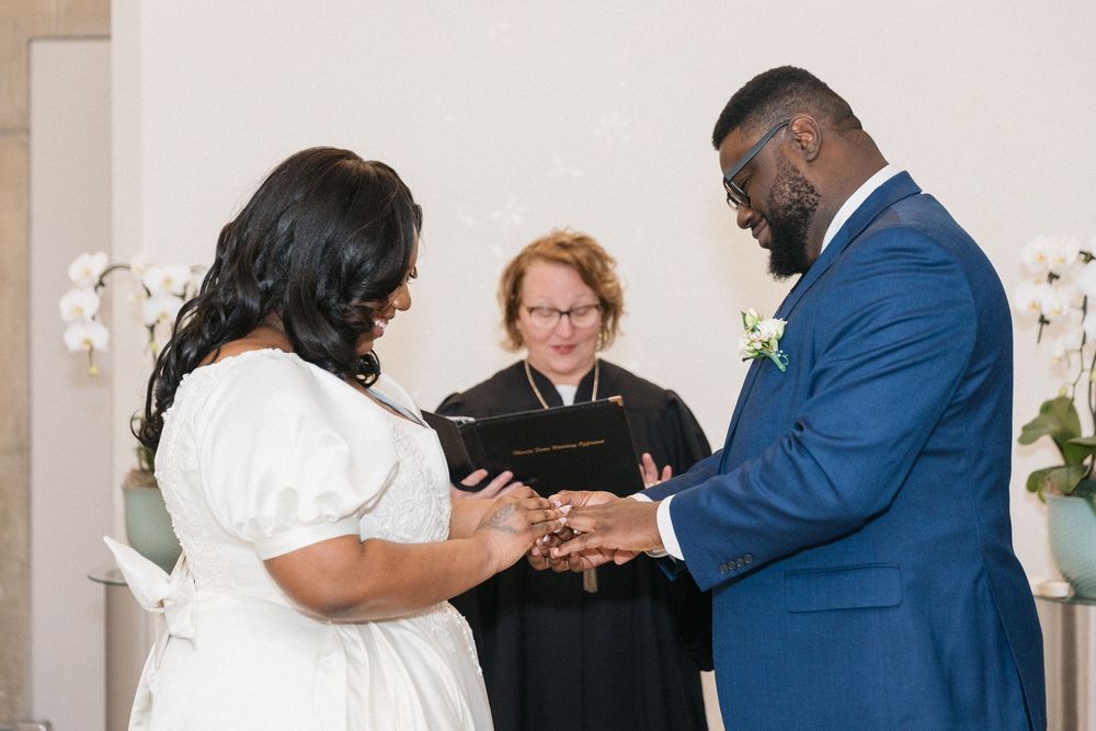 A couple in formal attire dances together at an elegant wedding reception in a white decorated venue.