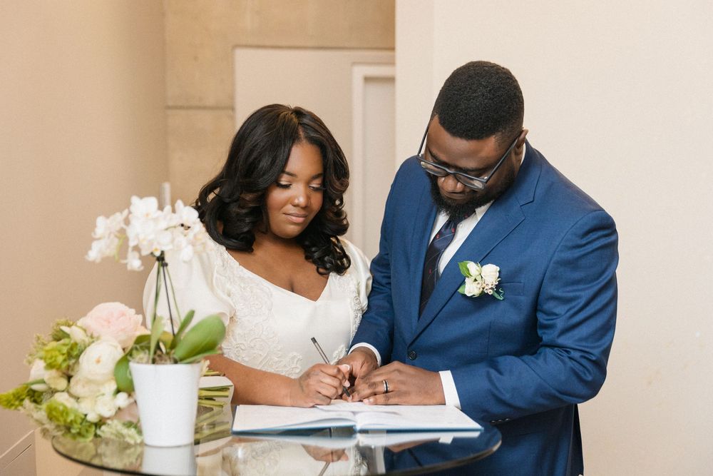 Couple in wedding attire signing marriage documents at a table with white orchids.