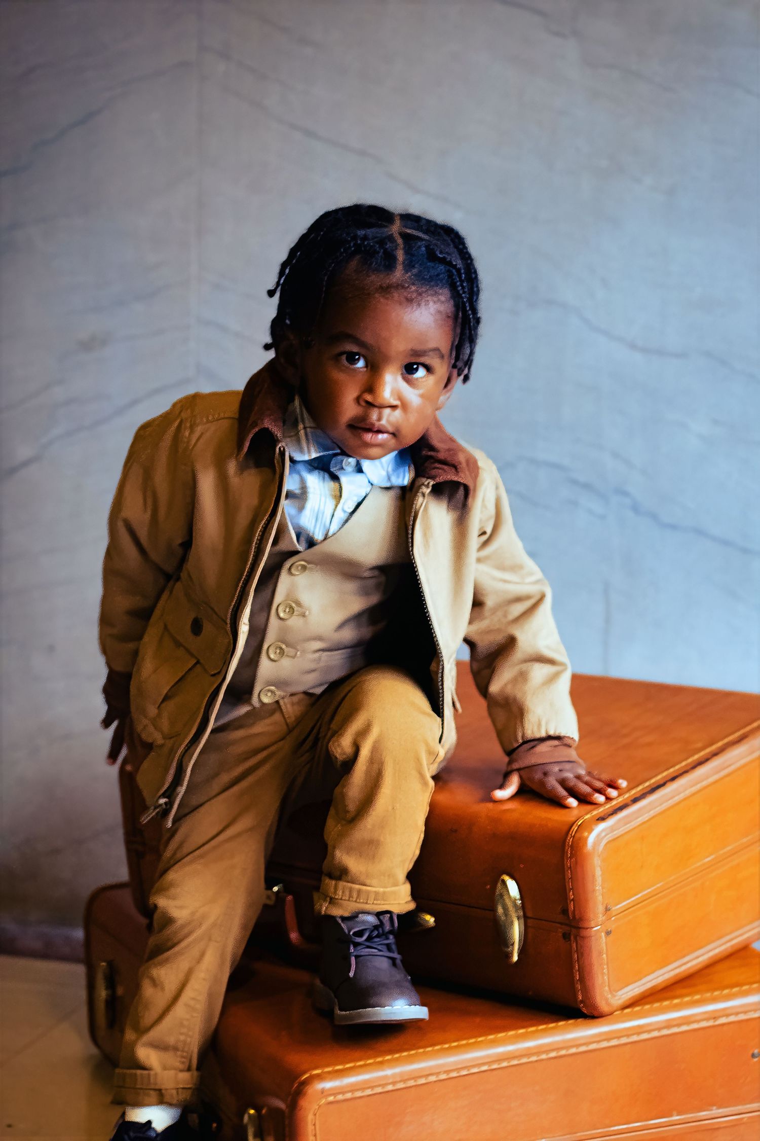 A toddler in beige overalls sits in a wooden courtroom chair while looking off to the side.