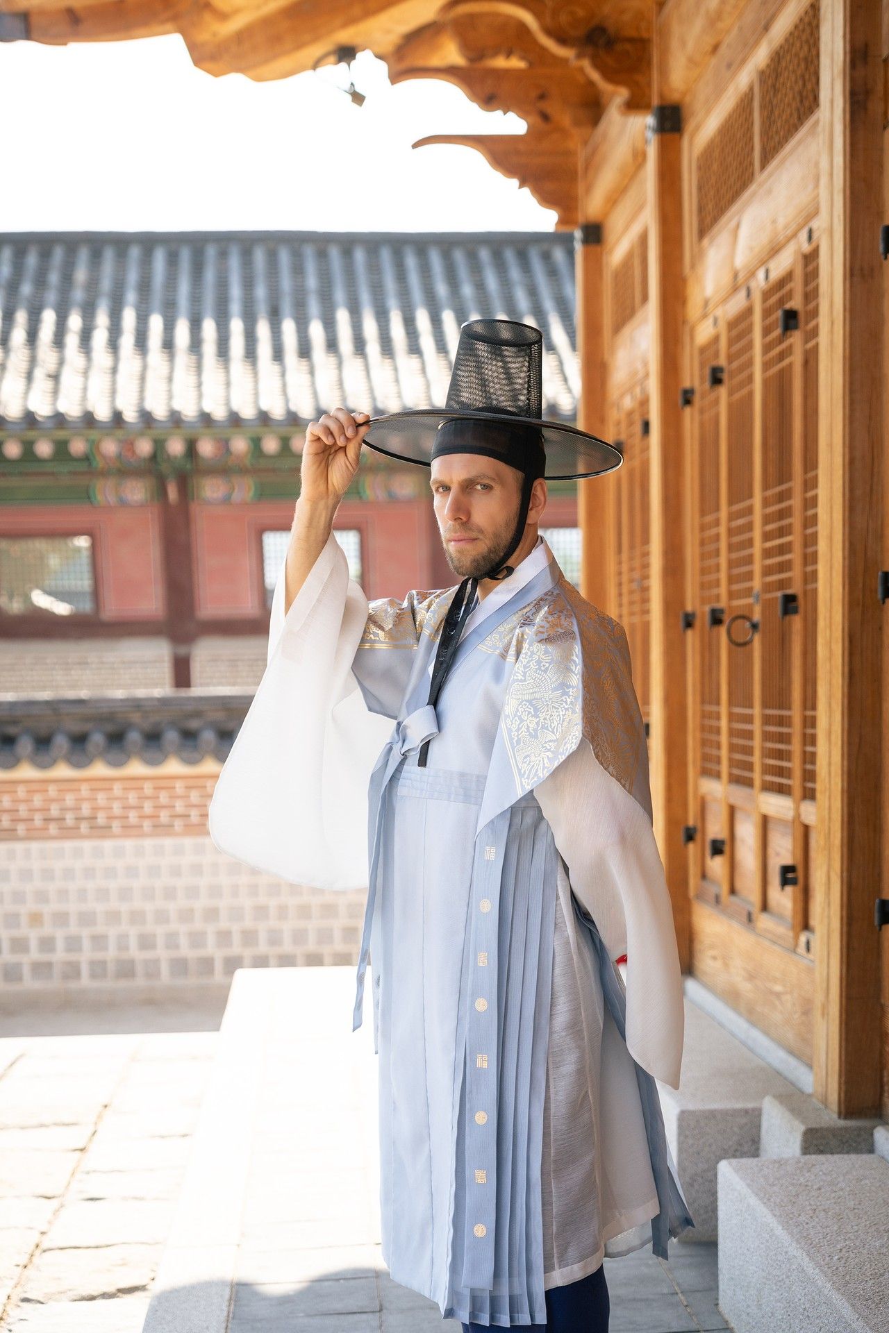 Traditional Korean hanbok and black hat worn in historic wooden palace architecture with ornate details.