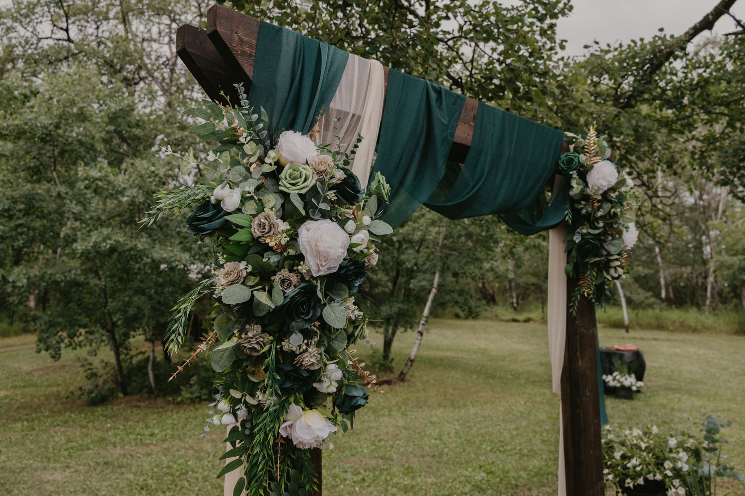 Elegant white floral wedding arch arrangements against natural outdoor backdrop.