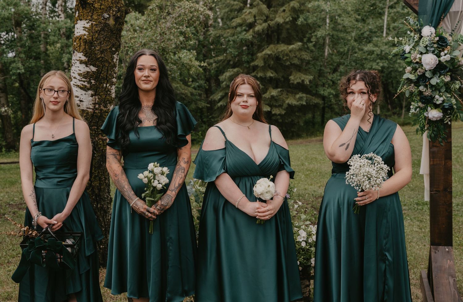 Row of bridesmaids in matching emerald green dresses at outdoor ceremony.
