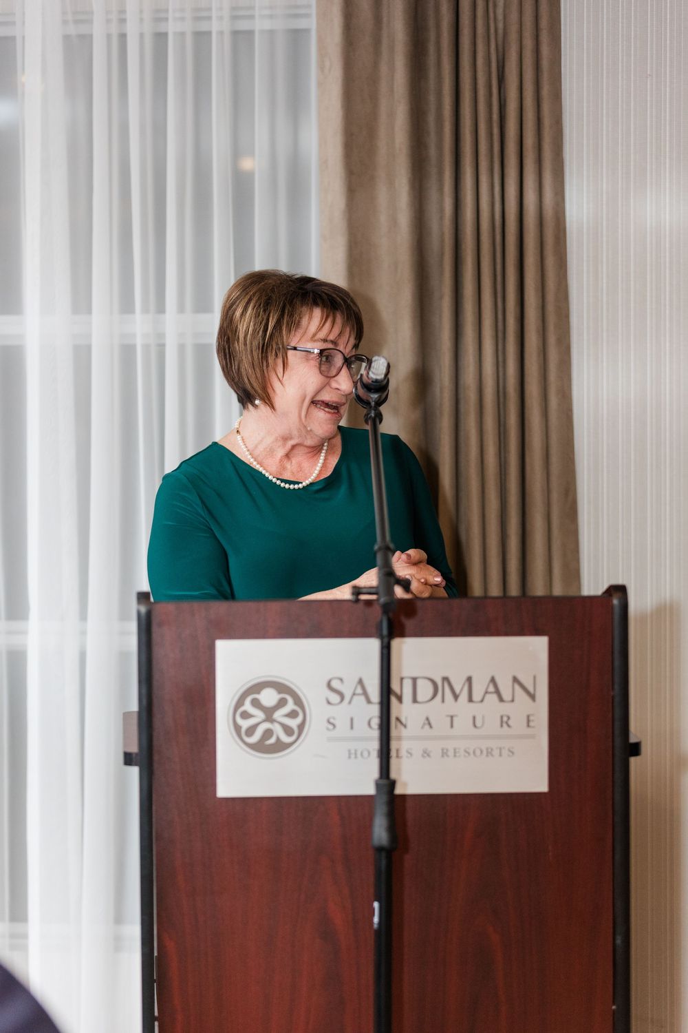 Speaker delivers remarks at a podium with Sandman Signature branding at an indoor event.