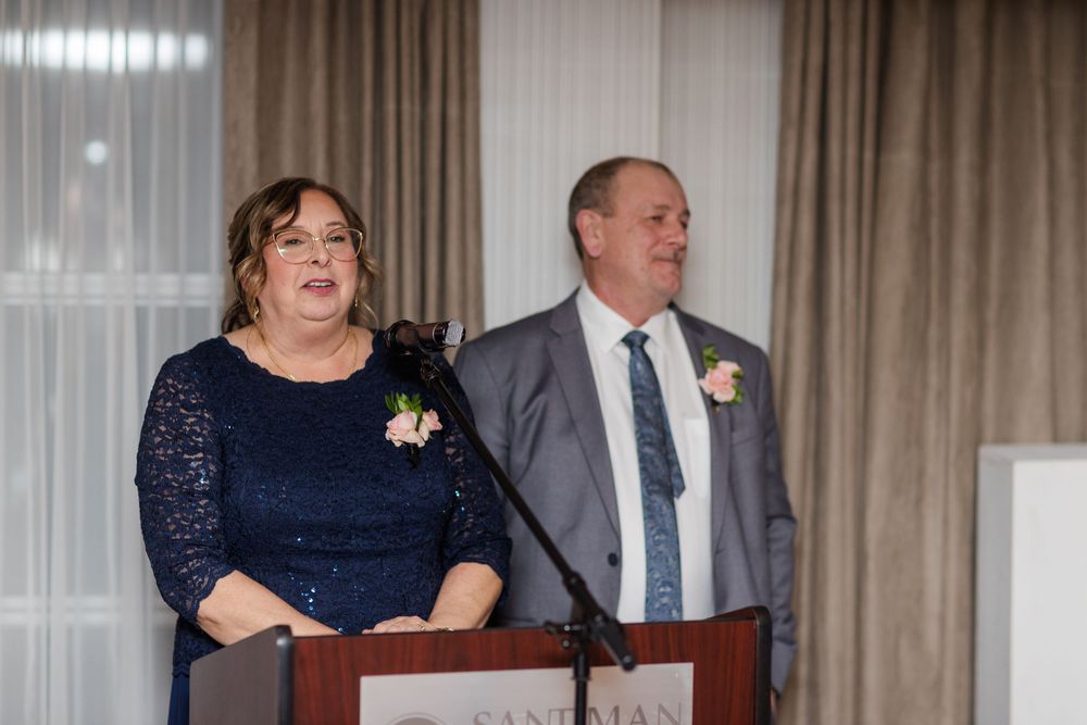 A couple in formal attire stands at a podium during what appears to be a wedding reception or formal event.