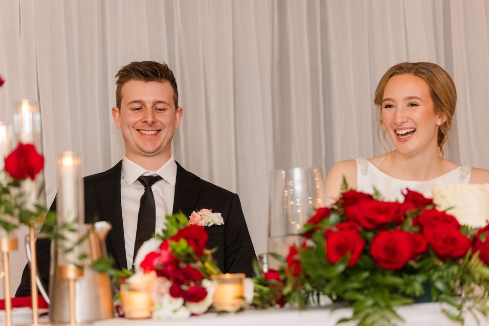 Wedding reception table decorated with elegant red roses and glowing candles in a white-draped venue.