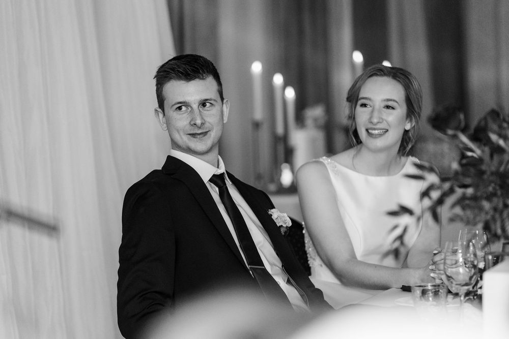 Wedding guests seated at a formal dinner table with candlelight and floral centerpieces.