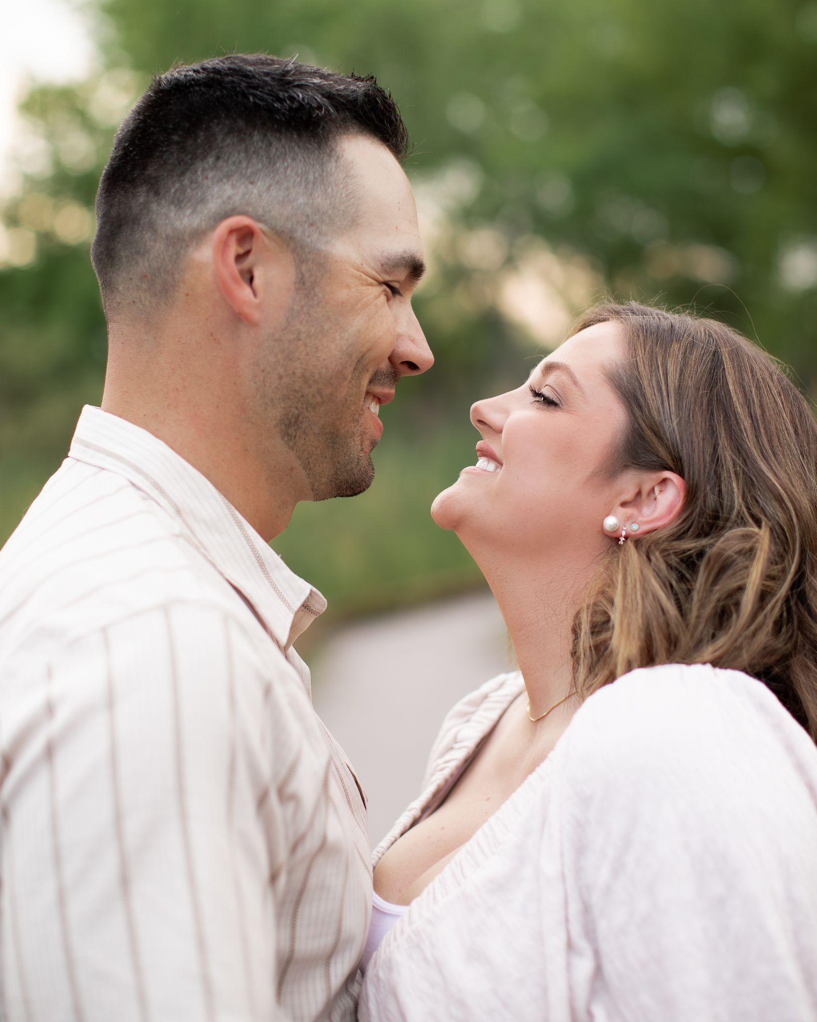 A couple in white clothing shares a romantic moment outdoors with a blurred green background.