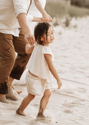 A child and adult walk together on a sandy beach, their feet leaving footprints in the soft white sand at Gilson Park