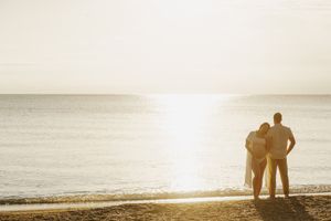 Silhouetted figures walk along a misty beach at sunset with soft golden light reflecting on the wet sand at maternity photoshoot in Kenosha.