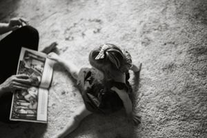 Black and white photo of a child lying on carpet while an adult reads a magazine nearby.