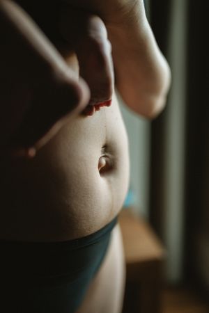 Close-up of a person's midsection showing stomach with belly button piercing and blue underwear waistband.