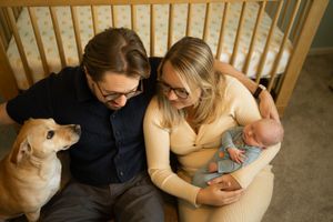 A couple sits on a couch with their dog while holding and feeding a baby in a warm, intimate home setting in Wilmette