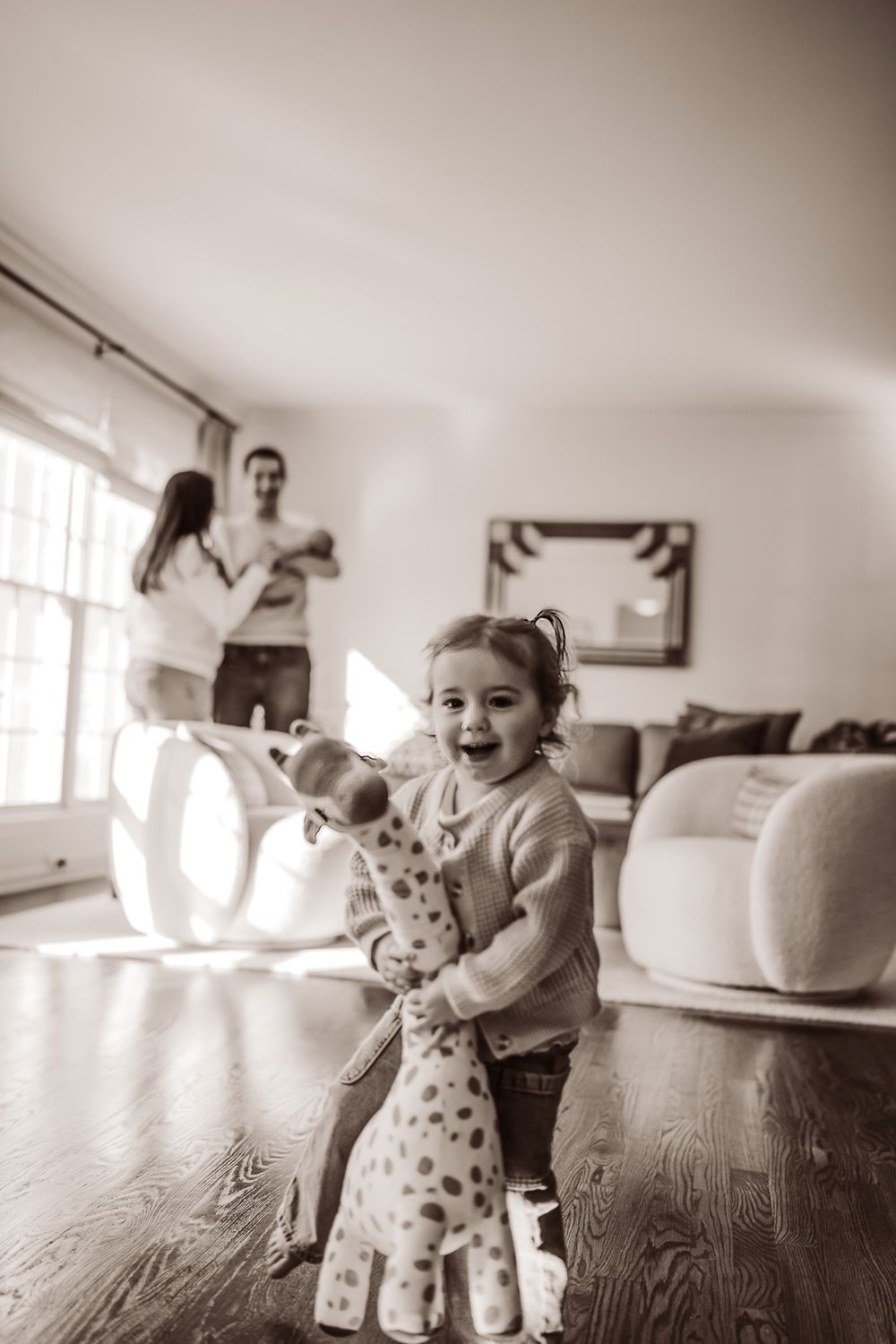 A black and white photo series showing a child playing and interacting with a large stuffed giraffe toy in a bright room.