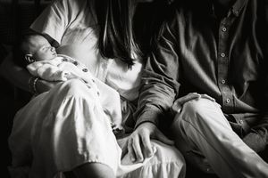 Black and white photo of parents cradling their newborn baby, a tender family moment captured in soft light.