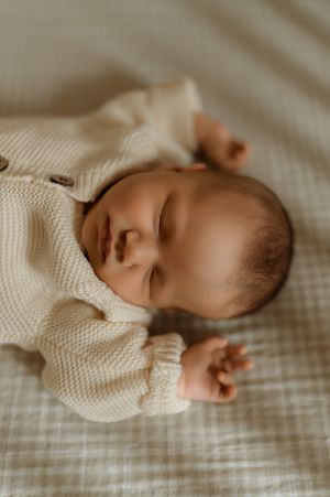 Sleeping newborn baby in cream knit onesie lying on soft checkered blanket.