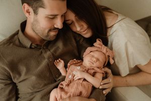 New parents tenderly hold their sleeping newborn baby dressed in pink, sharing an intimate forehead-to-forehead moment.