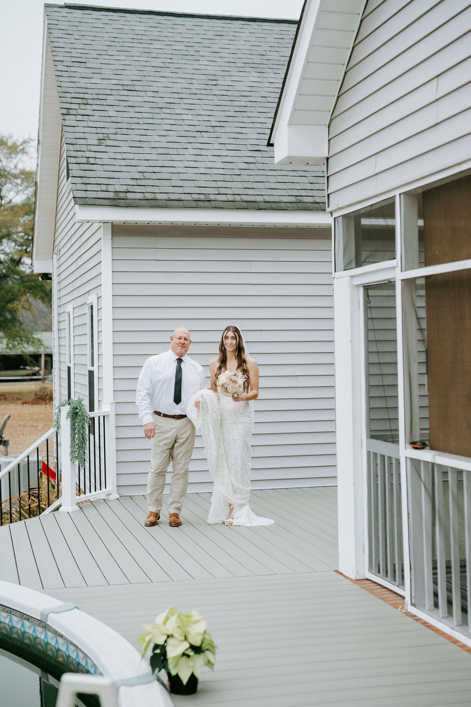 A couple shares a romantic moment on a white wooden deck during their wedding photoshoot.