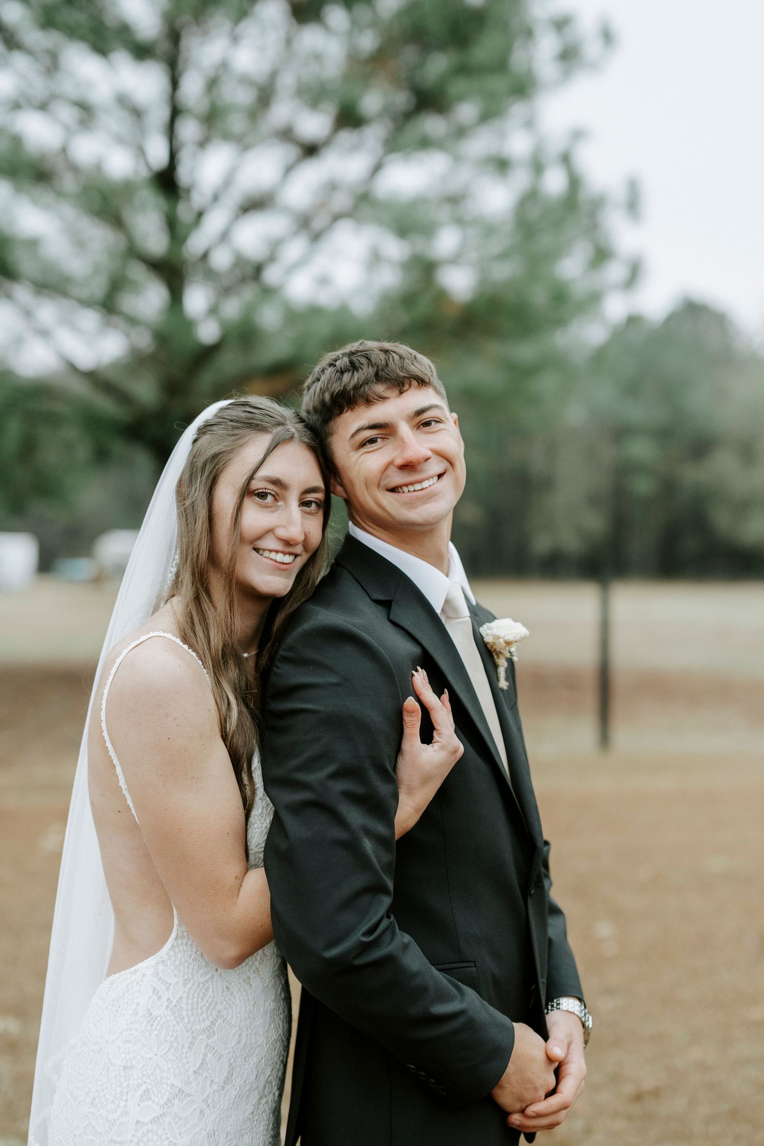 A couple shares an intimate moment in their wedding attire against a backdrop of pine trees.