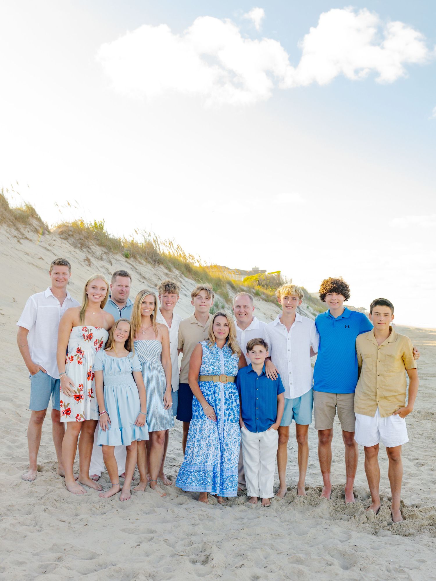 Large family group poses together on a sunny beach wearing coordinated blue and white outfits.