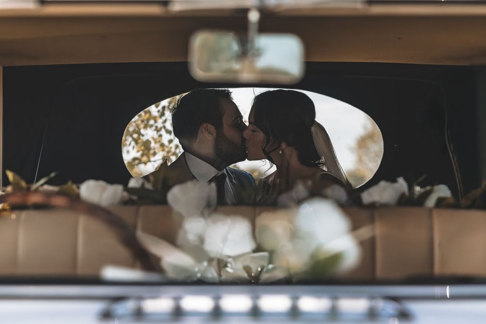 Relaxed wedding portrait of bride and groom sharing a kiss in the back of their wedding car.