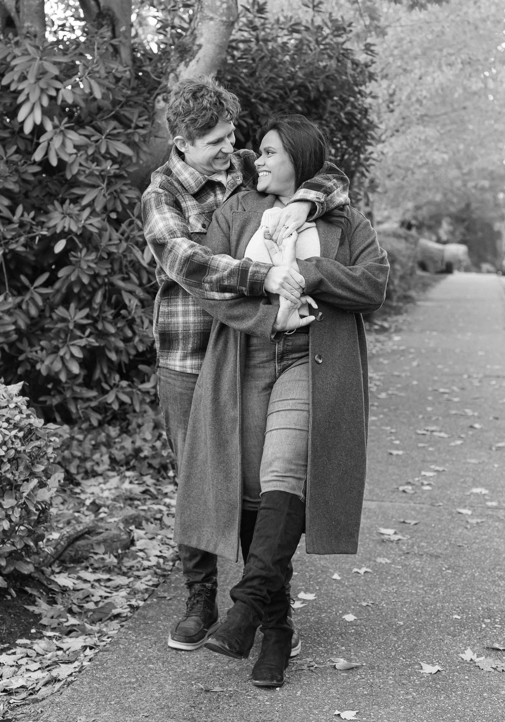 A romantic black and white photograph of a couple sharing an intimate moment on a leaf-strewn path in autumn.