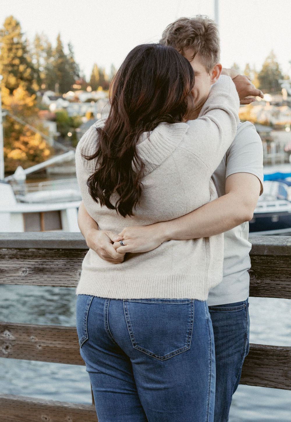 Couple embracing while standing by a waterfront dock during golden hour sunset.
