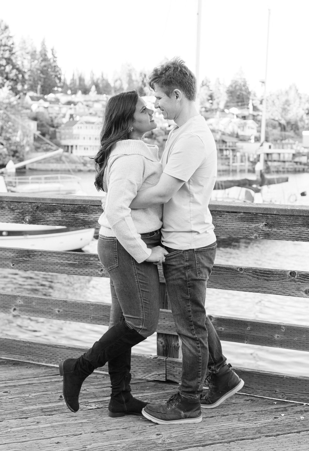 A romantic black and white photo of a couple embracing on a wooden dock with trees in the background.