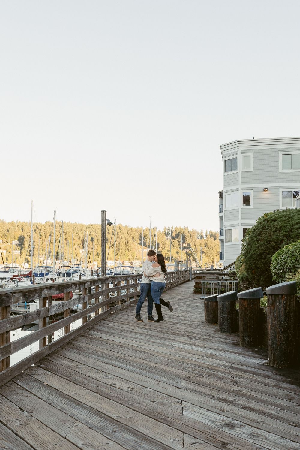 Wooden boardwalk along a marina with boats and buildings visible in the background at sunset.