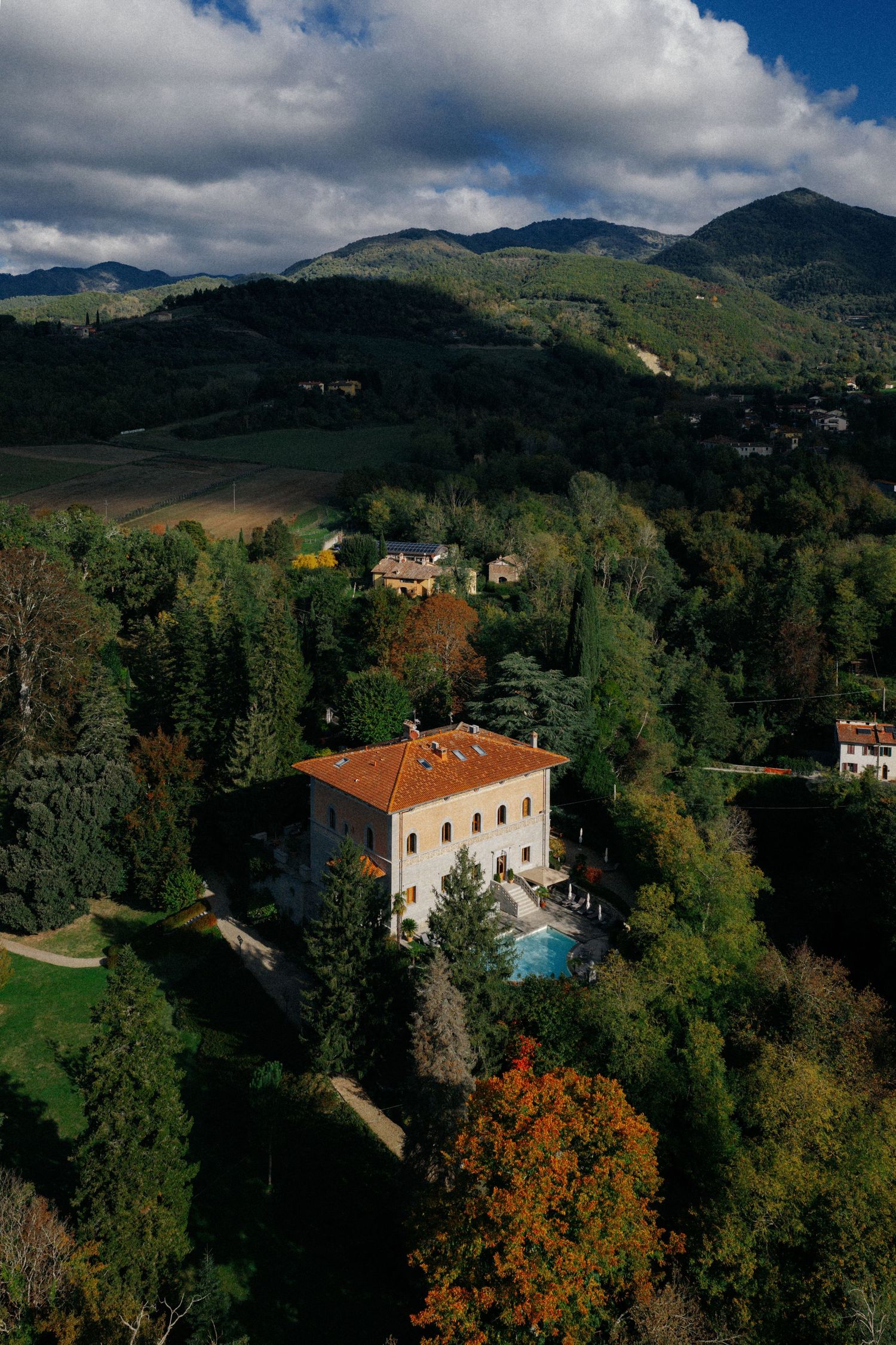 Aerial panoramic view of a luxury villa with swimming pool nestled in green hills and autumn trees in Tuscany.