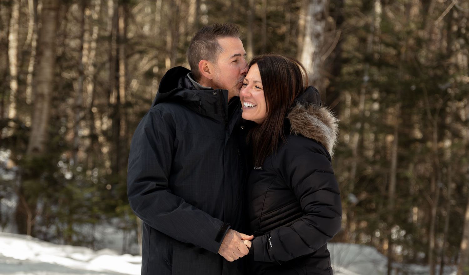 Couple sharing a joyful moment in snowy forest during winter.