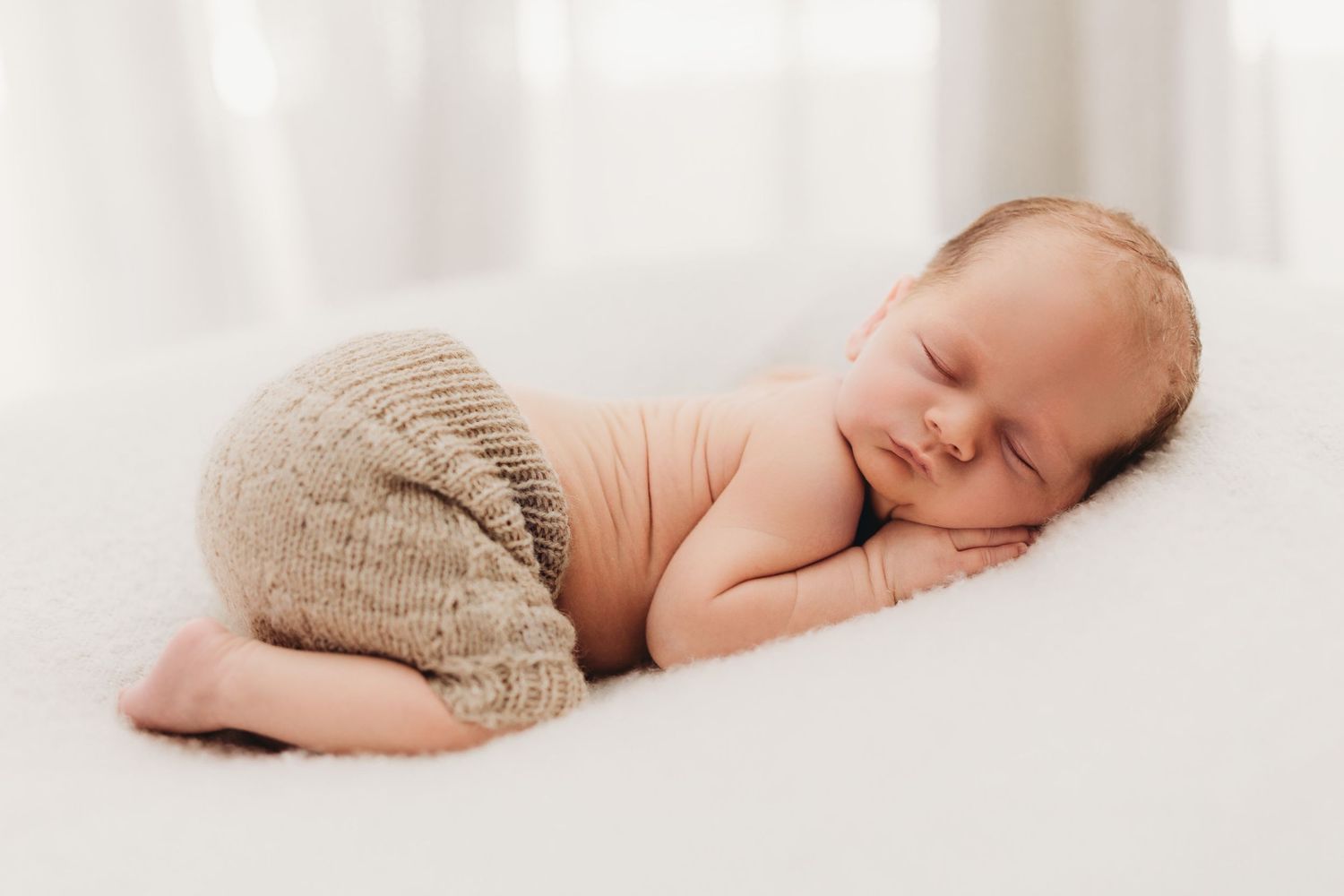 Sleeping newborn baby wearing knit pants on white backdrop.