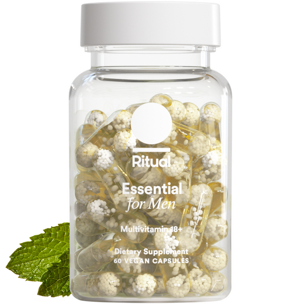 Glass jar filled with white and gold pill capsules next to fresh mint leaves on white background.