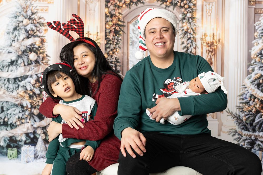 A family wearing burgundy and green sits together for holiday photos in front of decorated Christmas trees.