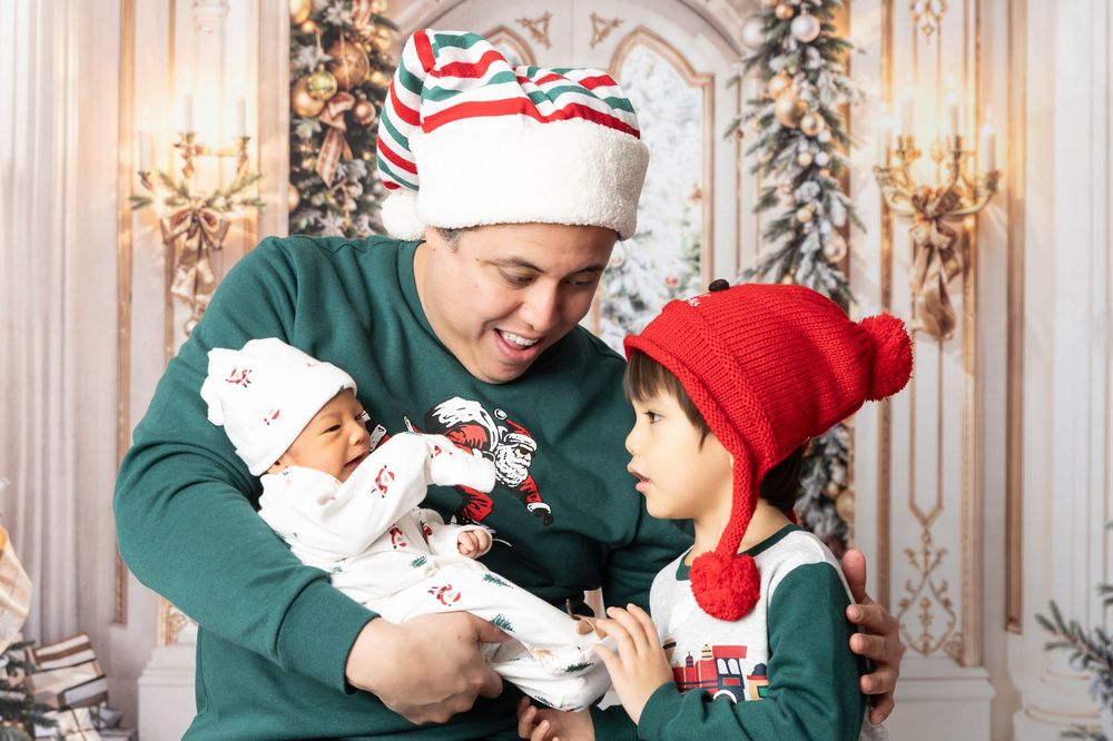 A festive holiday family moment with matching Christmas outfits and winter hats in front of a decorated backdrop.