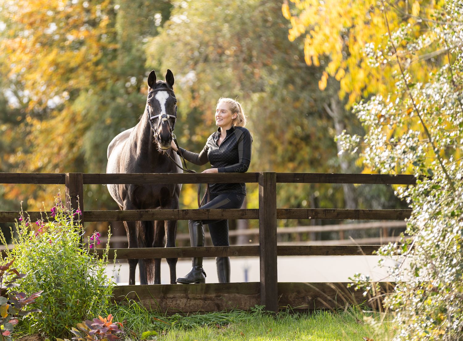 Two riders stand with their animals - a dog and a dark horse relaxing outdoors in a black and white photo.
