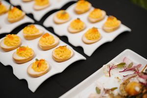 Rows of elegant orange-colored appetizers displayed on white serving spoons at an upscale event.