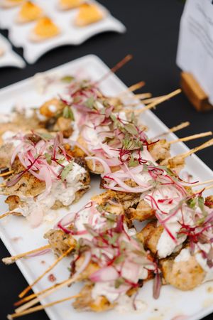 Grilled chicken skewers topped with pink pickled onions and fresh herbs served on white plates.