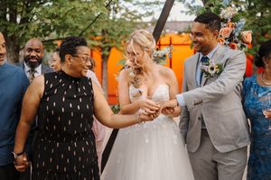 Wedding guests dance together outdoors under a canopy of trees with orange decorations in the background.