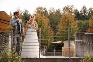 A couple stands together on a wooden deck overlooking autumn trees during a wedding ceremony at sunset.