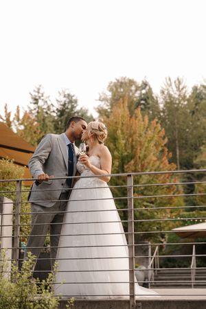 A romantic wedding couple shares intimate moments on a deck railing with autumn trees in the background.